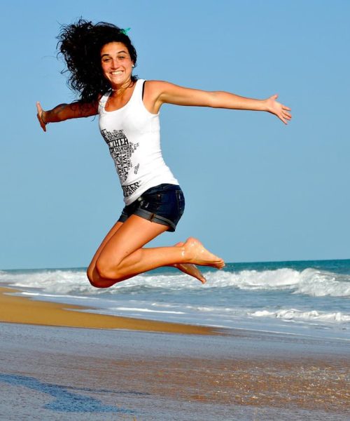 Sourire d'une femme sautant sur la plage ensoleillée.
