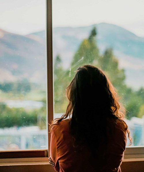 Sérieuse femme regardant par la fenêtre avec vue sur la nature et montagnes.
